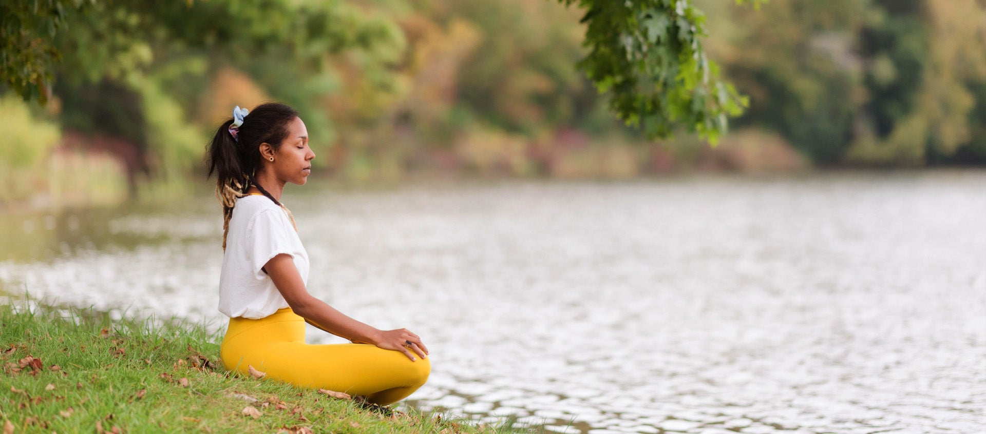 A woman of color meditates on the side of the lake at Kripalu