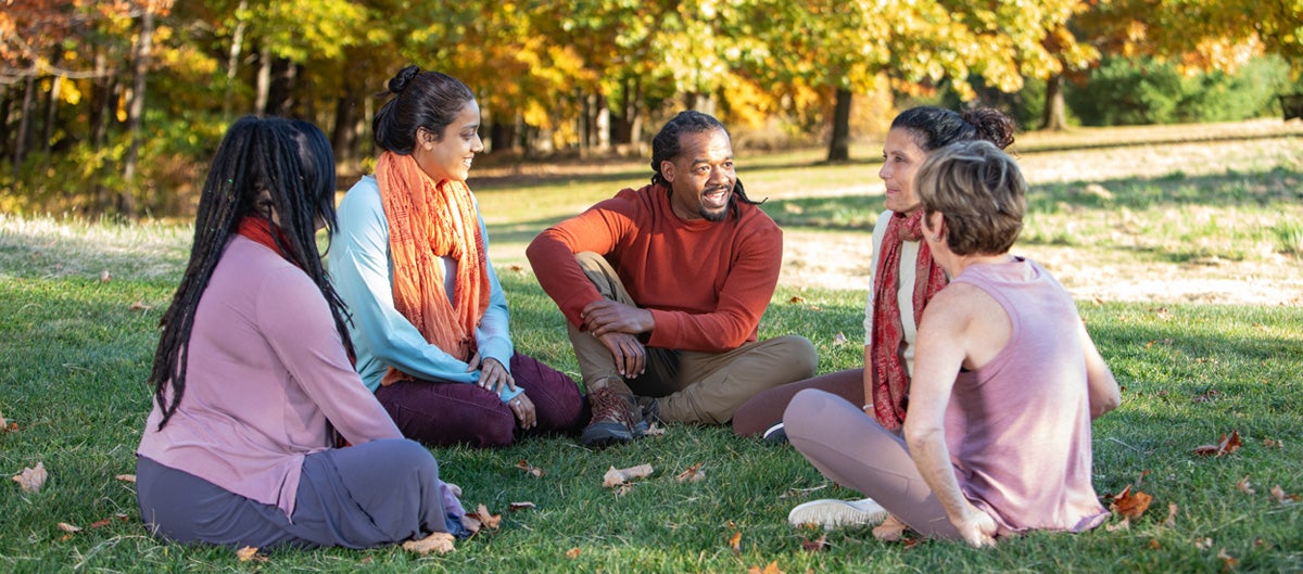 A diverse group of people stand in a field in Fall, their hands outstretched to the sky.
