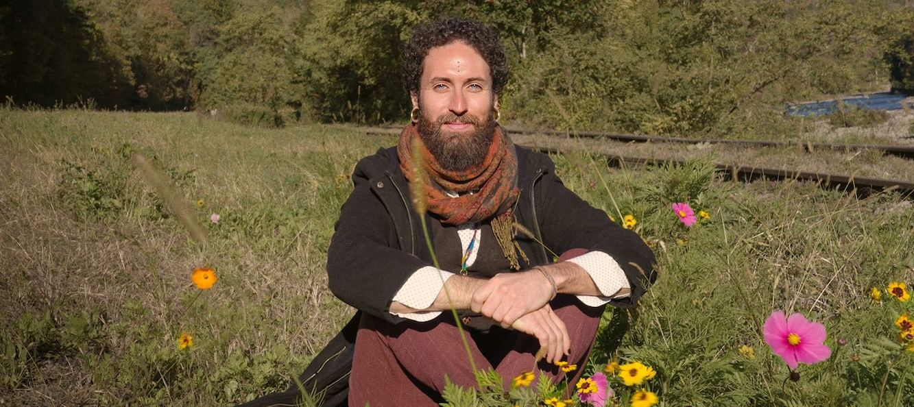 Luis Mojica sitting in a field with grass and flowers.
