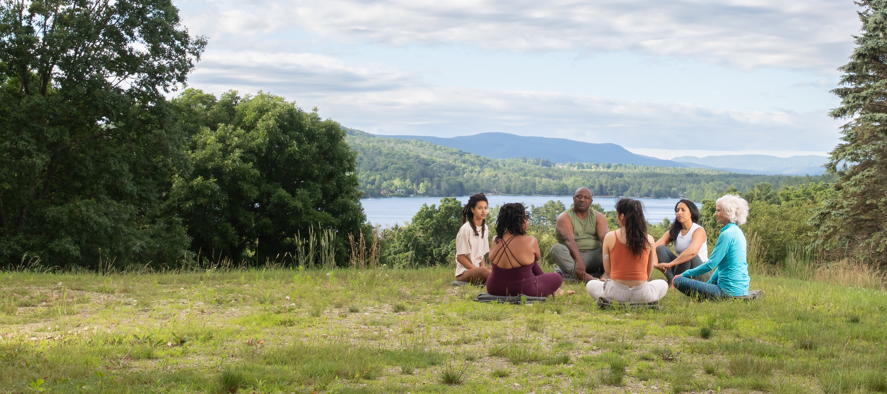 Group of people sitting in the grass on the Kripalu Campus with Lake Mahkeenac in the background