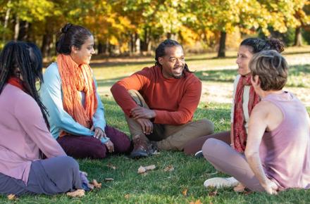 A diverse group of people stand in a field in Fall, their hands outstretched to the sky.
