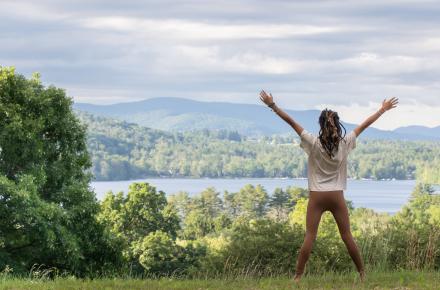 Woman with hands raised facing a lake and mountains in the Spring.