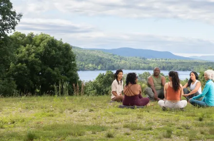 Group of people sitting in the grass on the Kripalu Campus with Lake Mahkeenac in the background