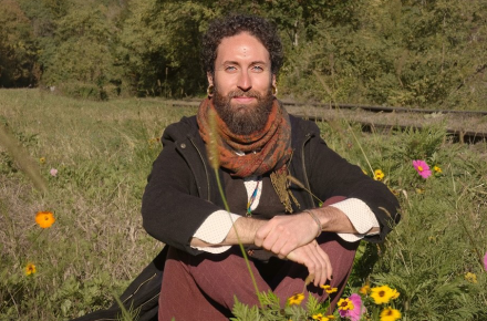 Luis Mojica sitting in a field with grass and flowers.