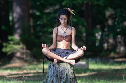 Woman meditating outdoors seated on a tree stump
