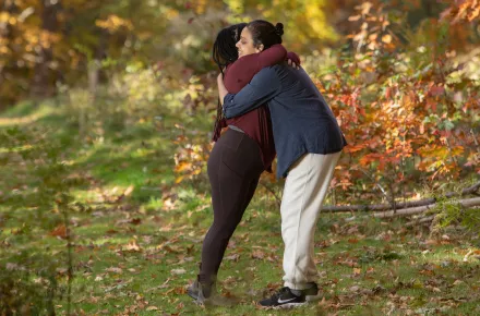Two women hugging in the woods in the fall.