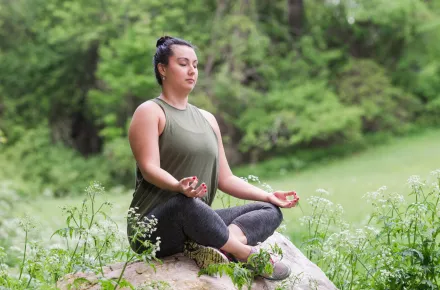 Woman sitting cross-legged on a rock meditating with eyes closed in the Spring.