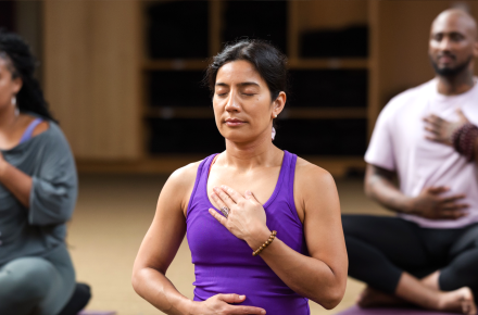 A class sits in meditation with their hands over their heart and stomach
