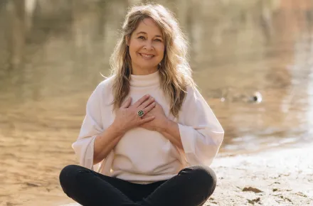 Renee Trudeau seated by a lake with hands over her heart
