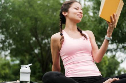 Young beautiful woman sitting outside smiling and holding a book