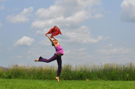 Woman in a field with arms raised, balancing on one foot