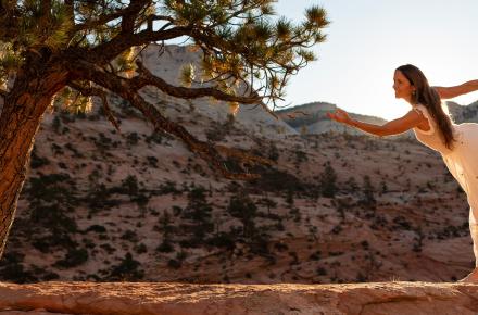 Kia Miller practicing yoga outdoors in a desert landscape next to a tree, with hills in the background