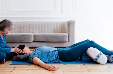Judith Lasater seated with her hands on the head of a woman lying on her back