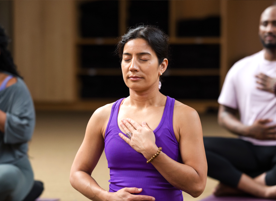 A class sits in meditation with their hands over their heart and stomach