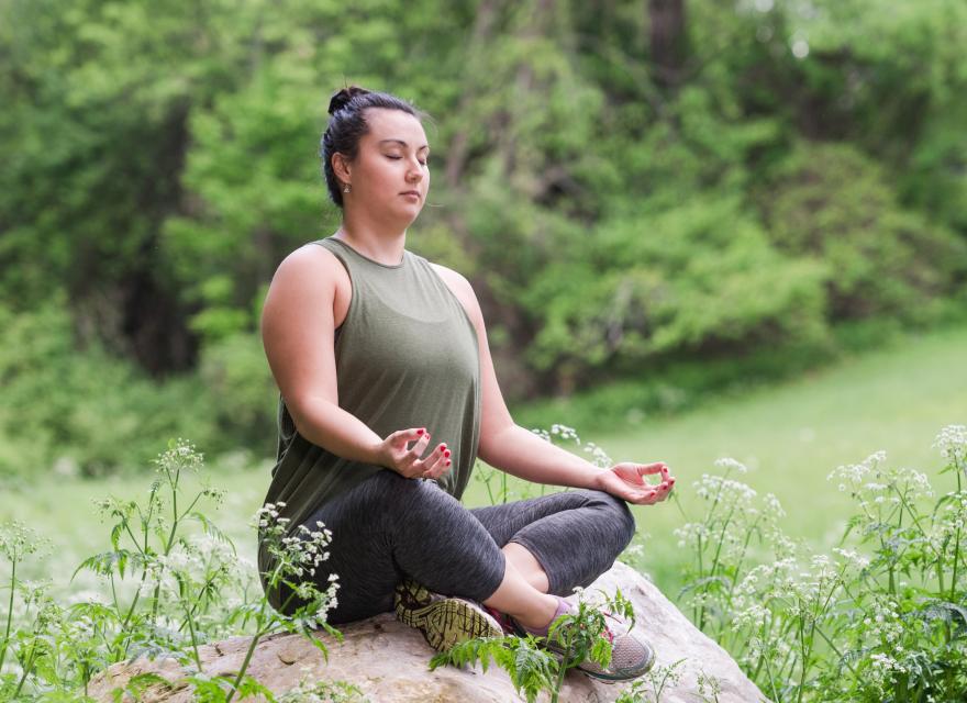Woman sitting cross-legged on a rock meditating with eyes closed in the Spring.