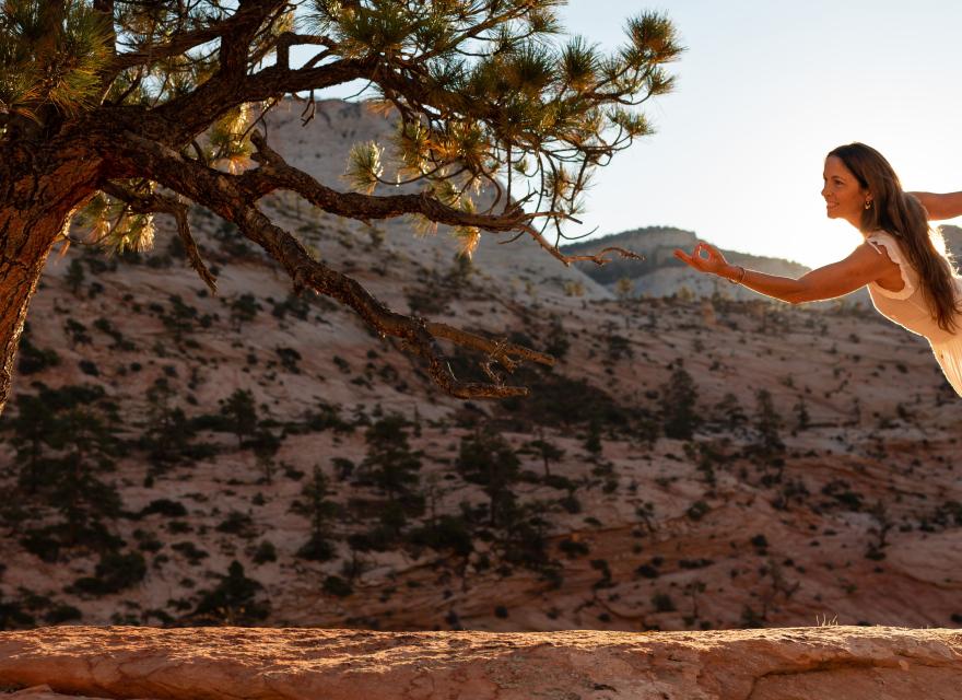 Kia Miller practicing yoga outdoors in a desert landscape next to a tree, with hills in the background