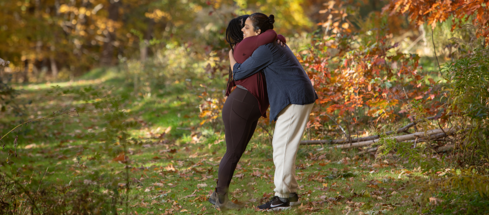 Rediscovering Us: A New Path to Connection, Presence, and Love Two women hugging in the woods in the fall.
