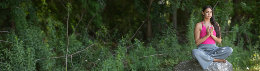 A woman meditates on a rock in the woods at Kripalu