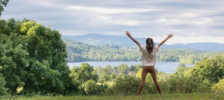 Woman with hands raised facing a lake and mountains in the Spring.