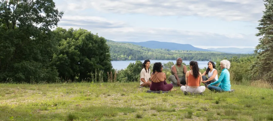 Group of people sitting in the grass on the Kripalu Campus with Lake Mahkeenac in the background