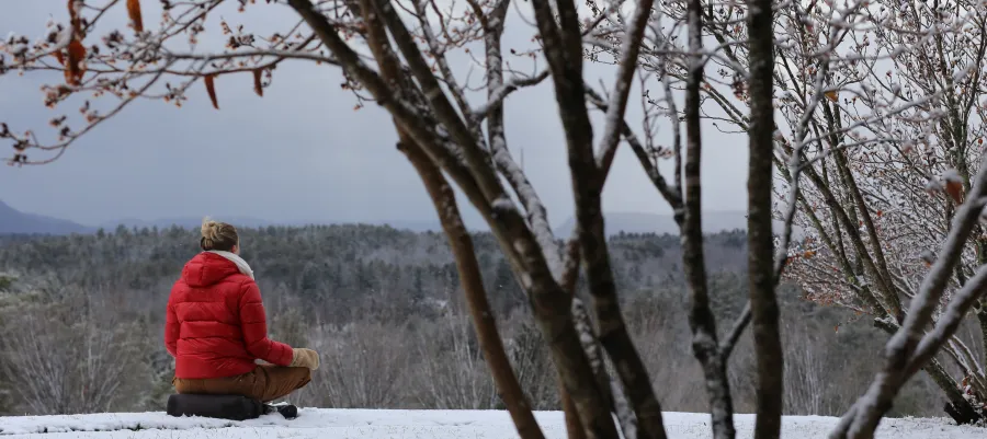 Woman in red jacket sitting on snowy ground looking out at the winter landscape.