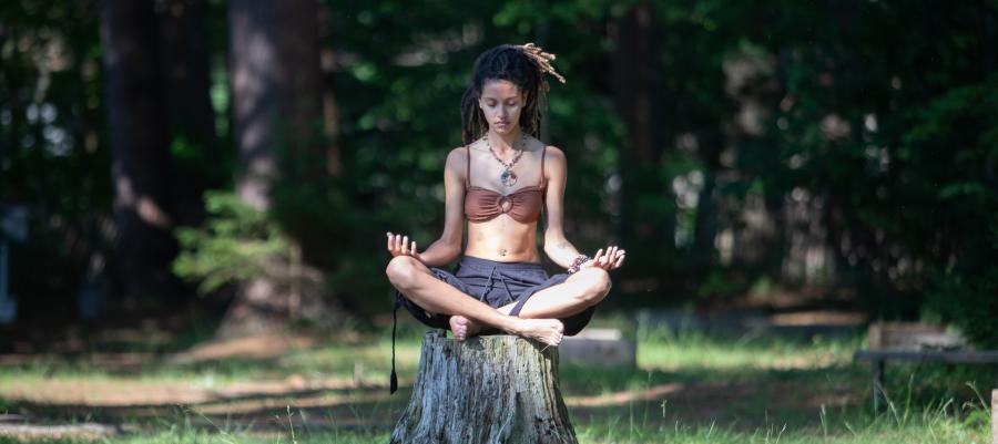 Woman meditating outdoors seated on a tree stump