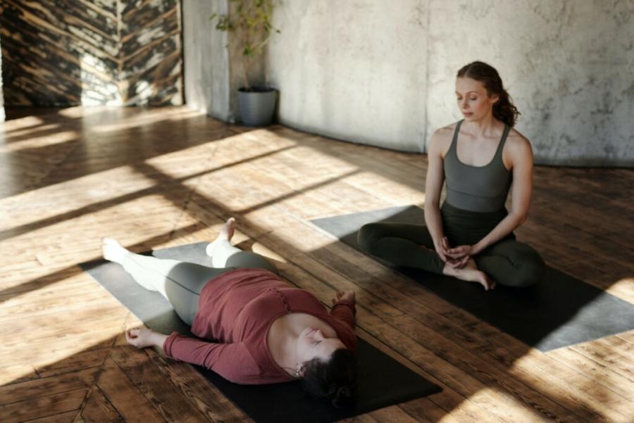 One woman seated on a yoga may, one woman lying on a yoga mat.