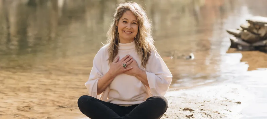 Renee Trudeau seated by a lake with hands over her heart
