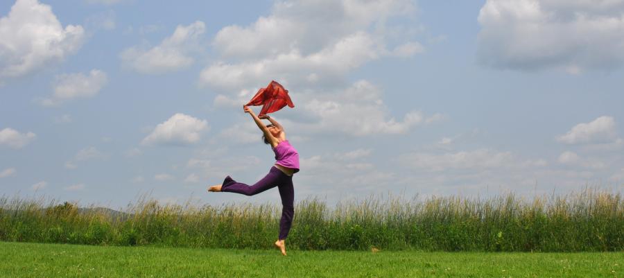 Woman in a field with arms raised, balancing on one foot