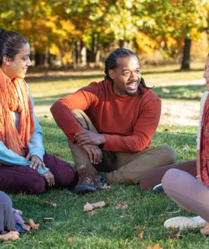 A diverse group of people stand in a field in Fall, their hands outstretched to the sky.