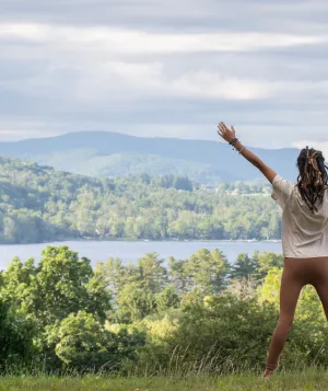 Woman with hands raised facing a lake and mountains in the Spring.