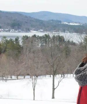 Woman standing with eyes closed outdoors in the winter with hills and lake in the background.