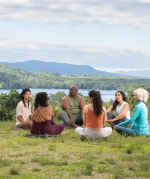 Group of people sitting in the grass on the Kripalu Campus with Lake Mahkeenac in the background