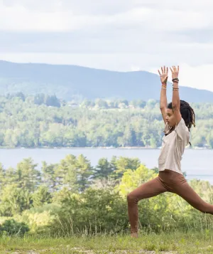 Woman with hands raised in a yoga pose next to a lake and mountains in the Summer