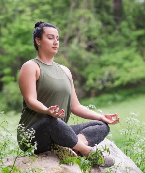Woman sitting cross-legged on a rock meditating with eyes closed in the Spring.