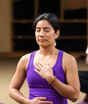 A class sits in meditation with their hands over their heart and stomach