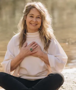 Renee Trudeau seated by a lake with hands over her heart