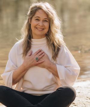 Renee Trudeau seated by a lake with hands over her heart