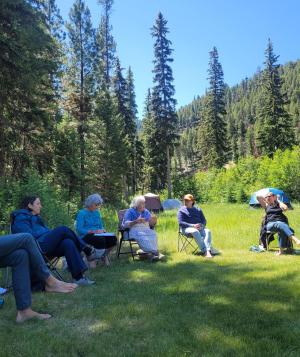 Group of people seated in chairs in a clearing in the woods.