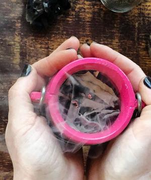 Hands holding a cup with burning incense