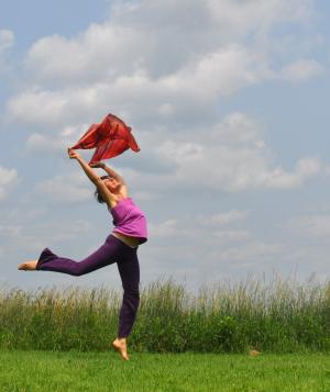 Woman in a field with arms raised, balancing on one foot